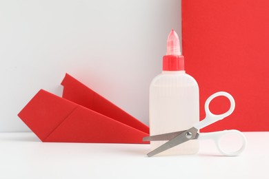 Photo of Glue, scissors and paper plane on white table against color background