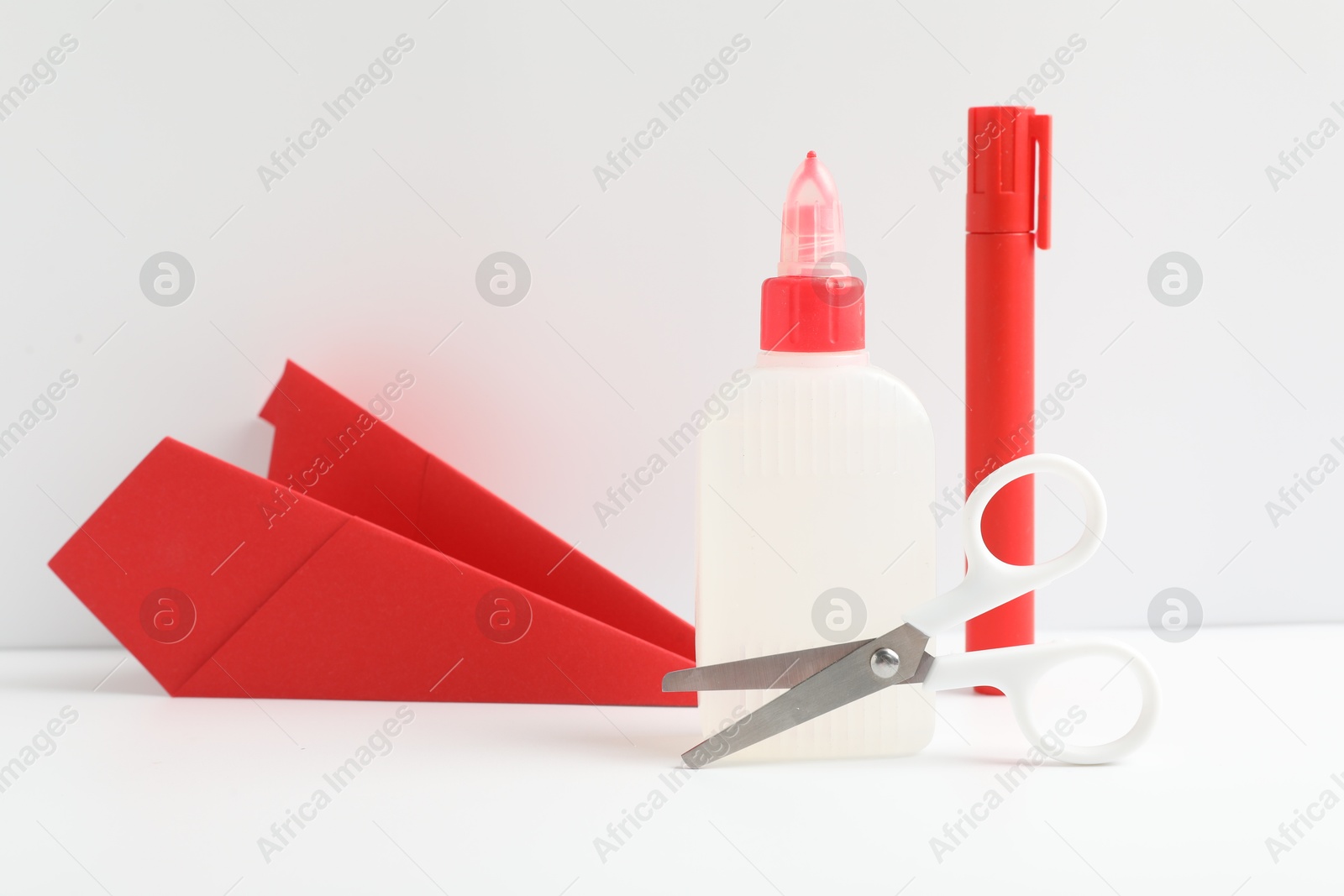 Photo of Glue, scissors, paper plane and marker on white table against color background