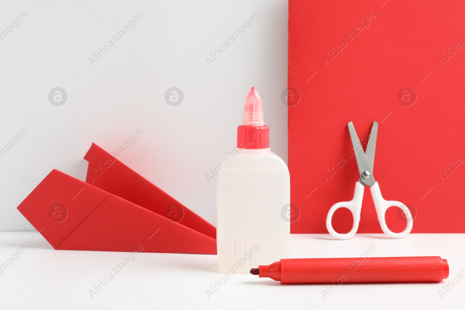 Photo of Glue, scissors, paper plane and marker on white table against color background