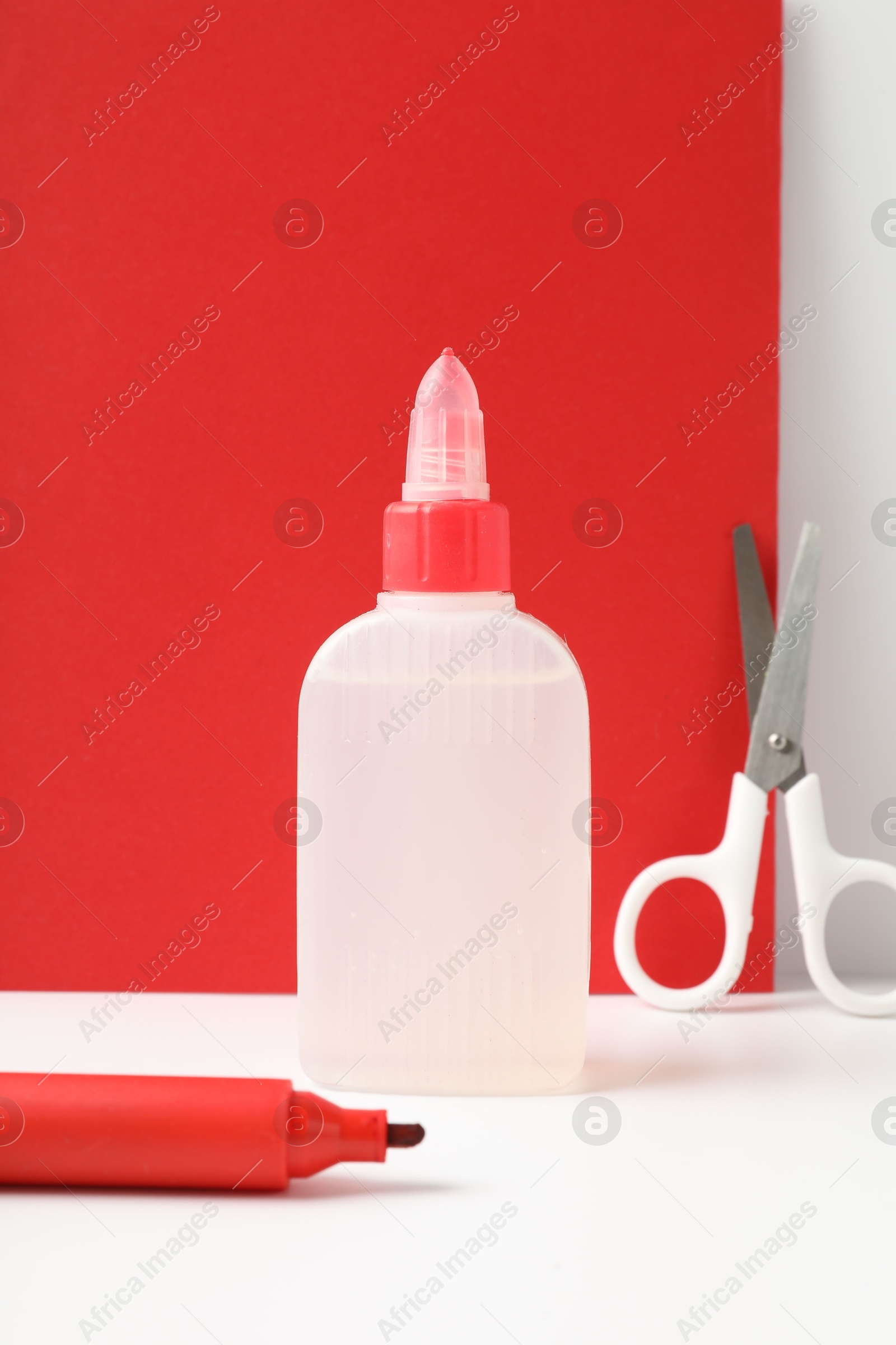 Photo of Glue, scissors and marker on white table against color background