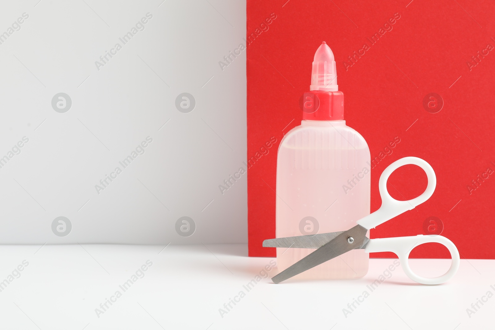 Photo of Glue and scissors on white table against color background. Space for text