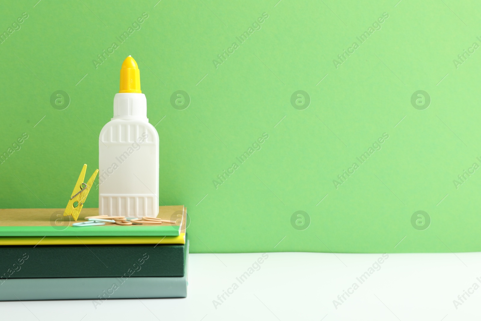 Photo of Glue and other stationery on white table against green background. Space for text