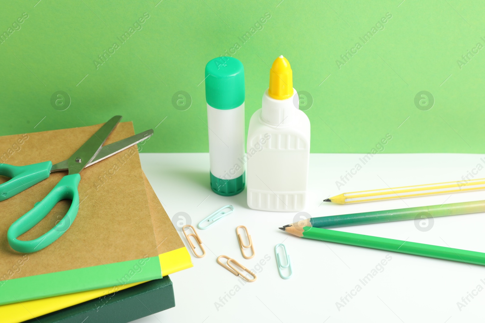 Photo of Glue and other stationery on white table against green background