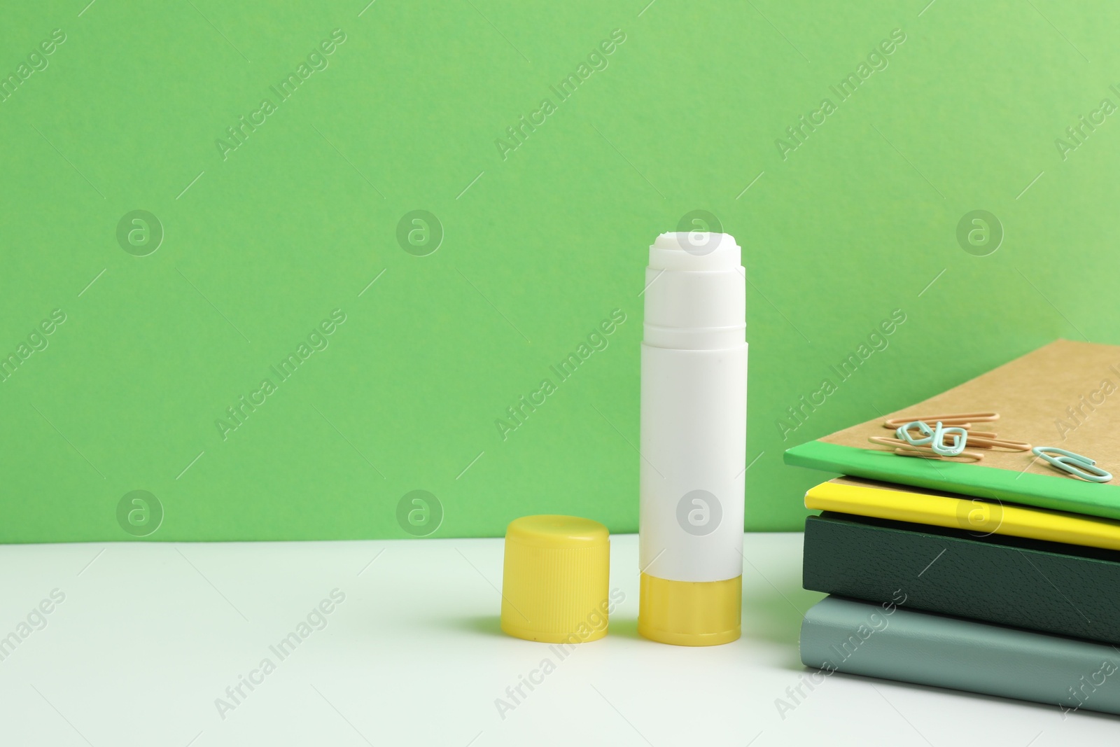 Photo of Glue and other stationery on white table against green background. Space for text
