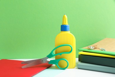 Photo of Glue, scissors and other stationery on white table against green background. Space for text