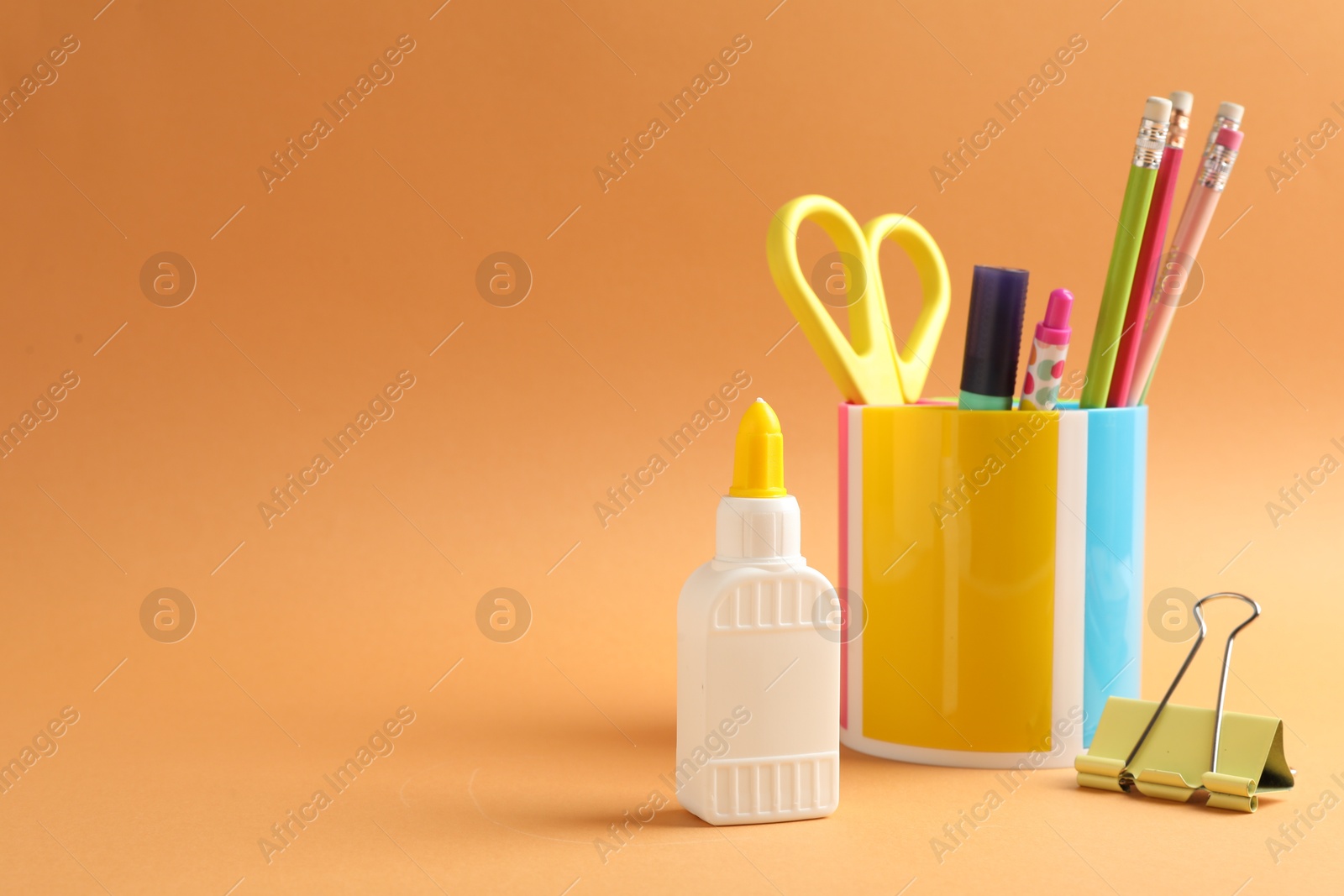 Photo of Glue and other stationery on pale orange background. Space for text
