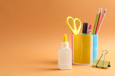 Photo of Glue and other stationery on pale orange background. Space for text