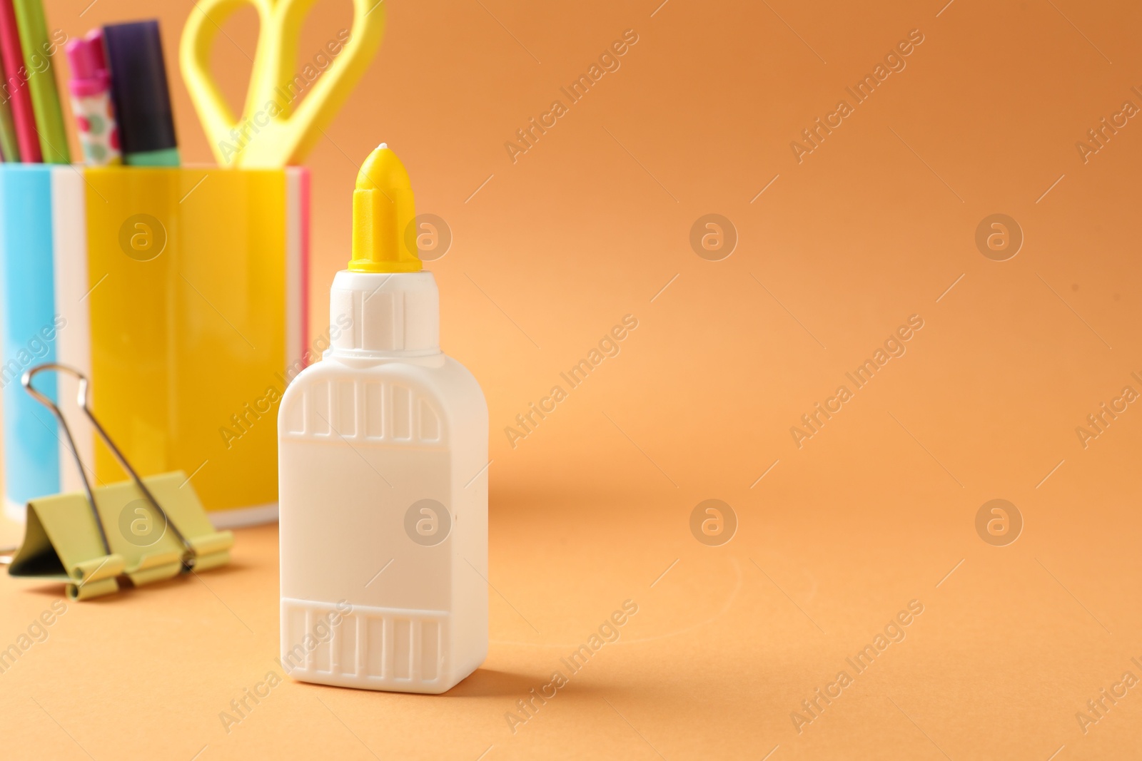 Photo of Glue and other stationery on pale orange background. Space for text