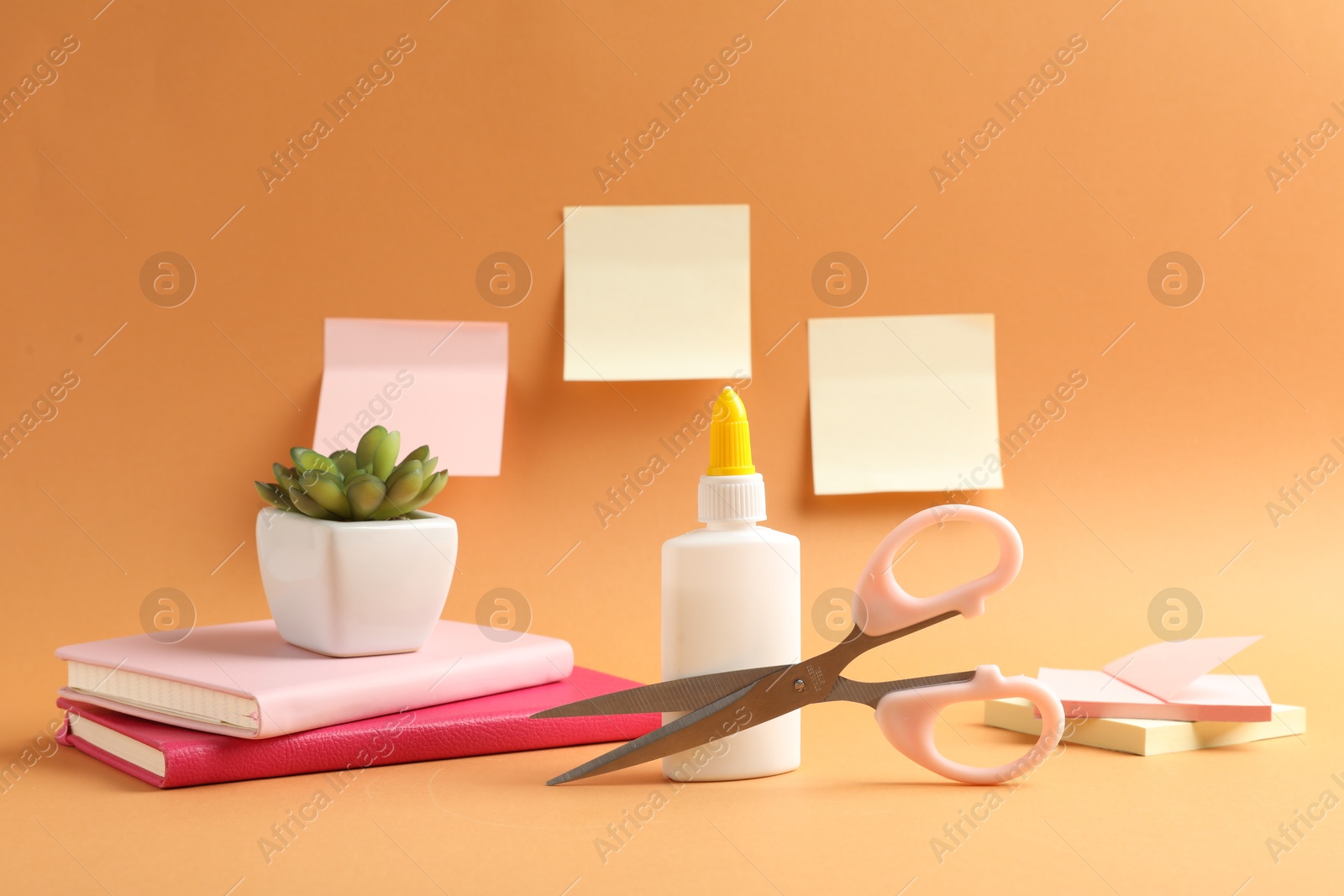 Photo of Glue, scissors and other stationery on pale orange background
