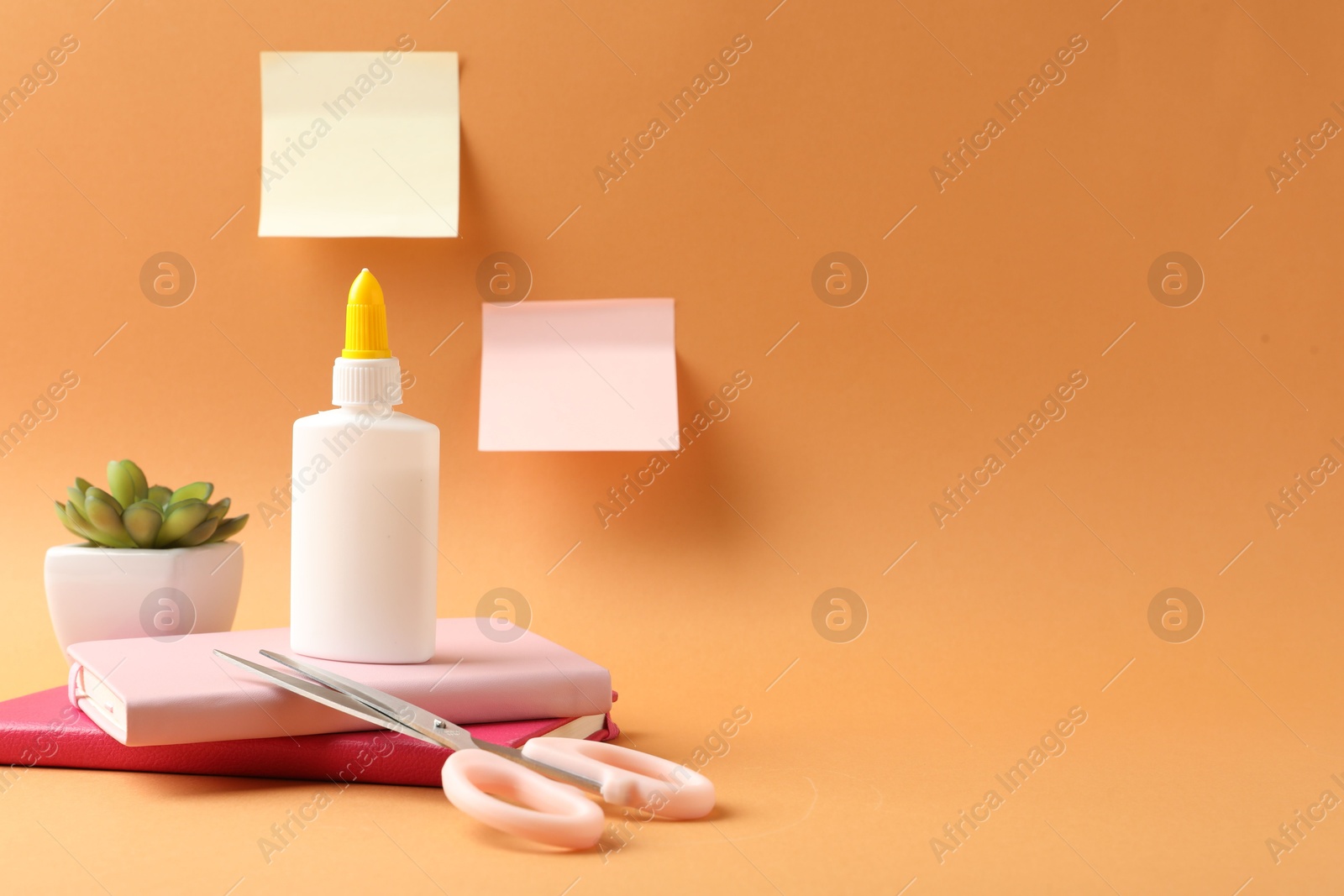 Photo of Glue and other stationery on pale orange background. Space for text