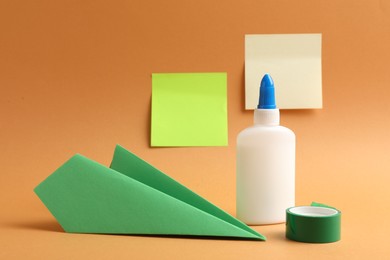 Photo of Glue, adhesive tape and paper plane on pale orange background