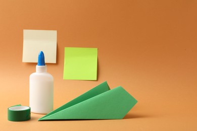 Photo of Glue, adhesive tape and paper plane on pale orange background. Space for text
