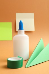 Photo of Glue, adhesive tape and paper plane on pale orange background
