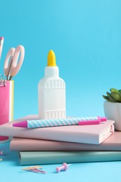 Photo of Glue and other stationery on light blue background, closeup