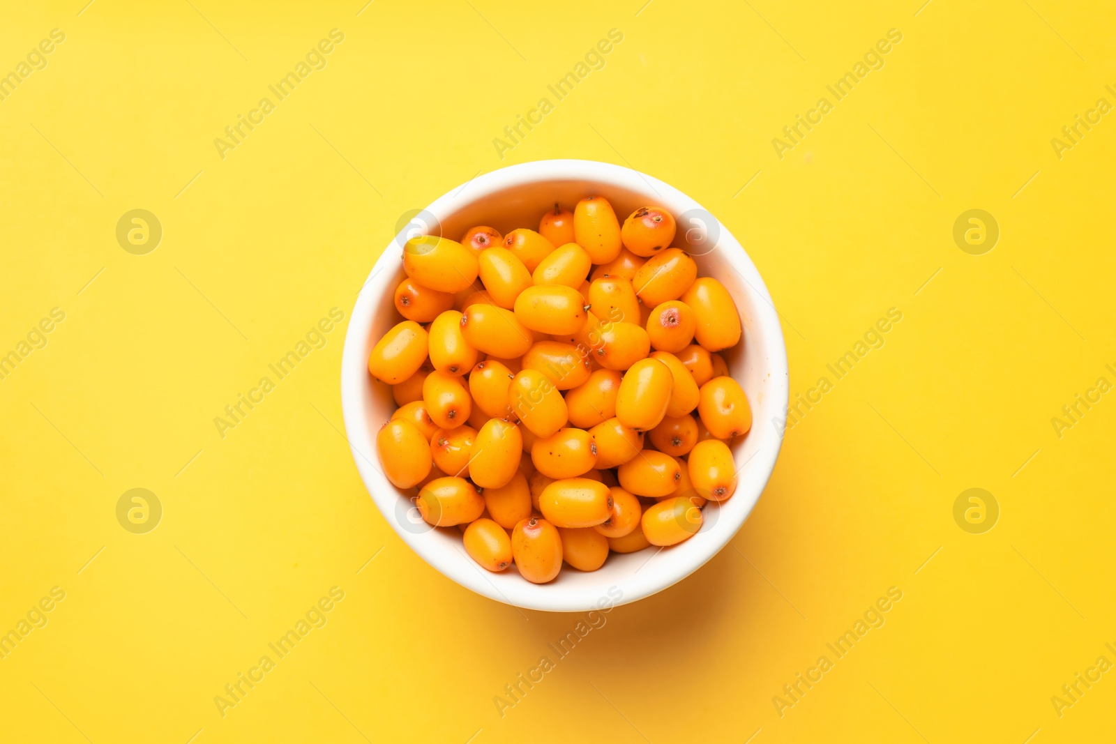 Ripe sea buckthorn berries in bowl on yellow background, top view Photo of Ripe sea buckthorn berries in bowl on yellow background, top view