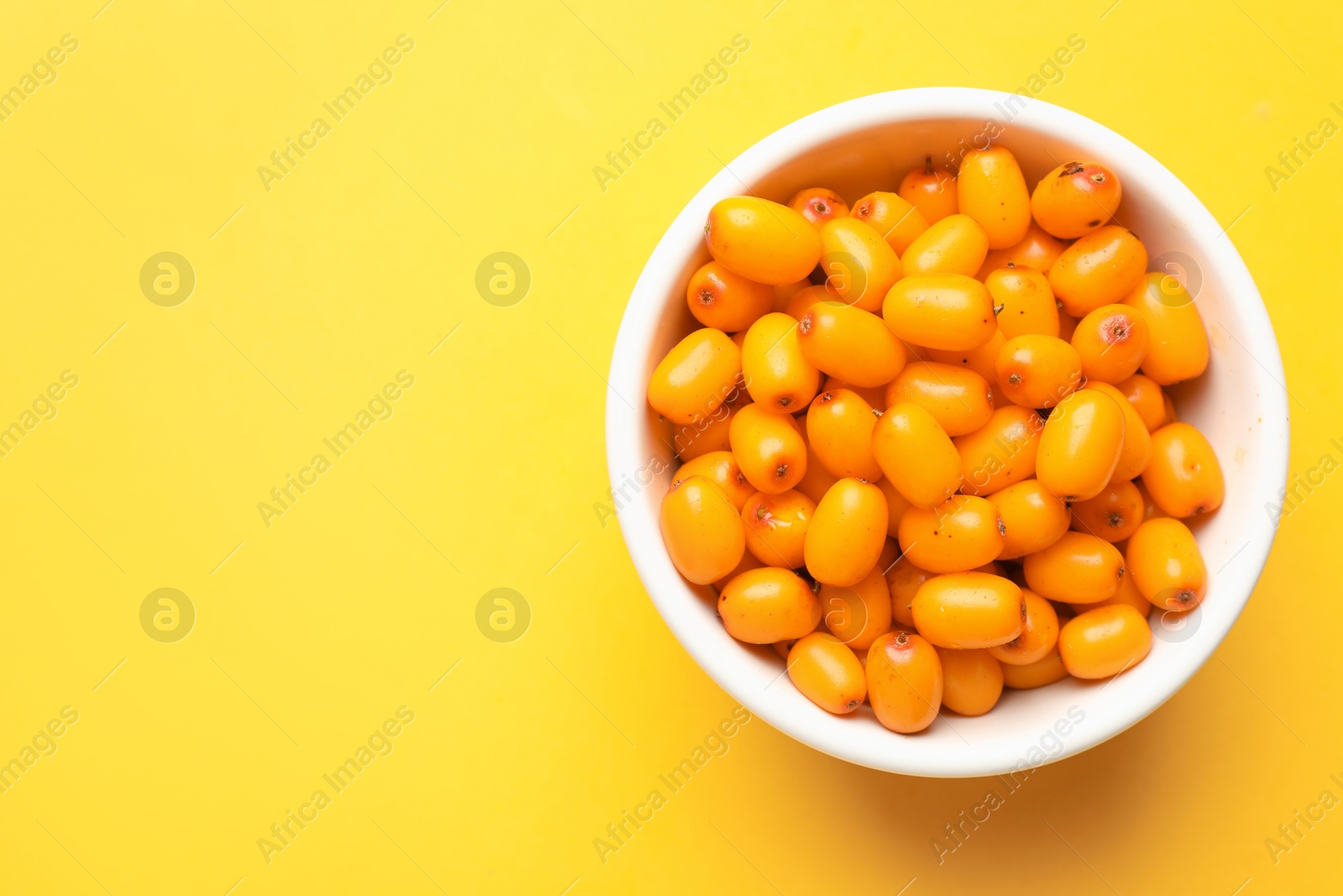 Ripe sea buckthorn berries in bowl on yellow background, top view. Space for text Photo of Ripe sea buckthorn berries in bowl on yellow background, top view. Space for text