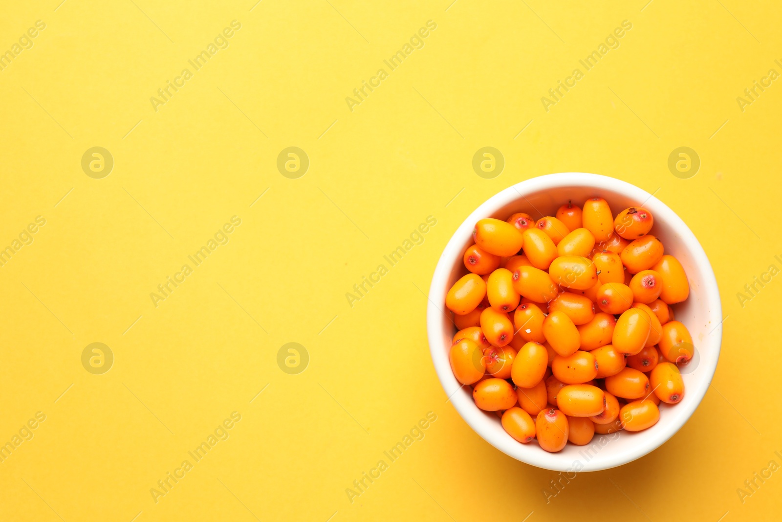 Ripe sea buckthorn berries in bowl on yellow background, top view. Space for text Photo of Ripe sea buckthorn berries in bowl on yellow background, top view. Space for text