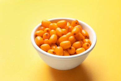 Photo of Ripe sea buckthorn berries in bowl on yellow background, closeup