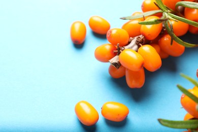 Photo of Branch with ripe sea buckthorn berries and leaves on light blue background, closeup. Space for text