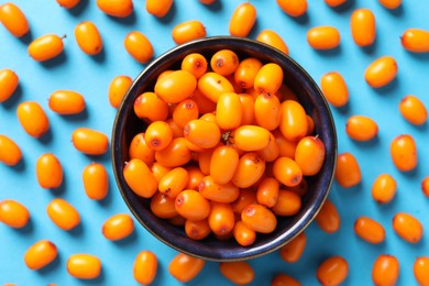 Photo of Ripe sea buckthorn berries and bowl on light blue background, flat lay