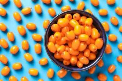 Photo of Ripe sea buckthorn berries and bowl on light blue background, flat lay