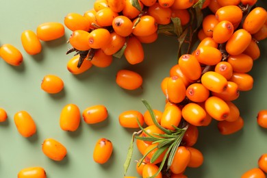 Photo of Branches with ripe sea buckthorn berries and leaves on green background, flat lay