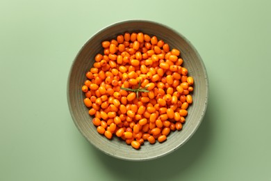 Photo of Ripe sea buckthorn berries and leaves in bowl on green background, top view