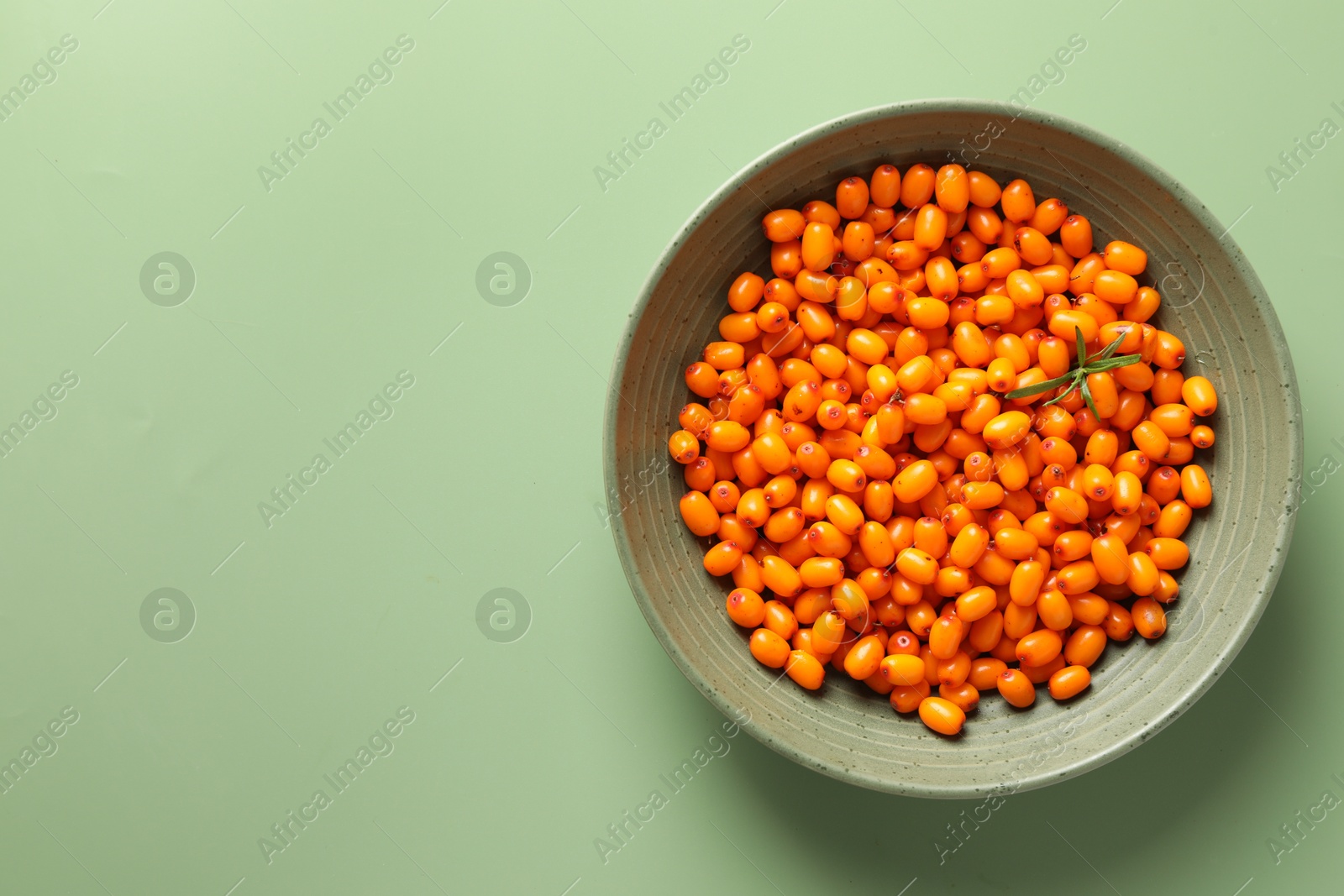 Photo of Ripe sea buckthorn berries and leaves in bowl on green background, top view. Space for text