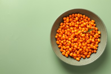 Photo of Ripe sea buckthorn berries and leaves in bowl on green background, top view. Space for text