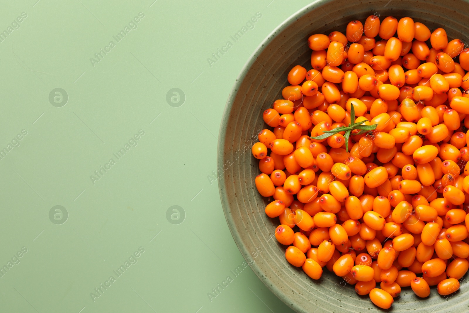 Photo of Ripe sea buckthorn berries and leaves in bowl on green background, top view. Space for text