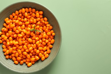 Photo of Ripe sea buckthorn berries and leaves in bowl on green background, top view. Space for text