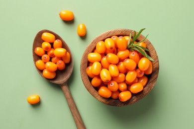 Photo of Ripe sea buckthorn berries, bowl and spoon on green background, flat lay
