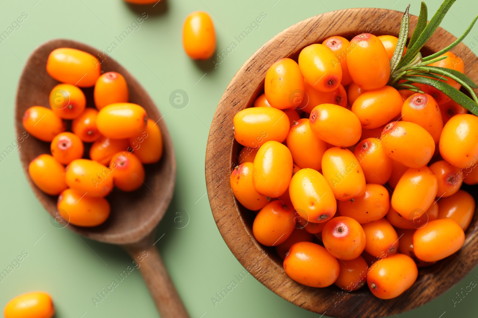 Photo of Ripe sea buckthorn berries, bowl and spoon on green background, flat lay