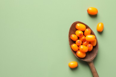 Photo of Ripe sea buckthorn berries and spoon on green background, flat lay. Space for text