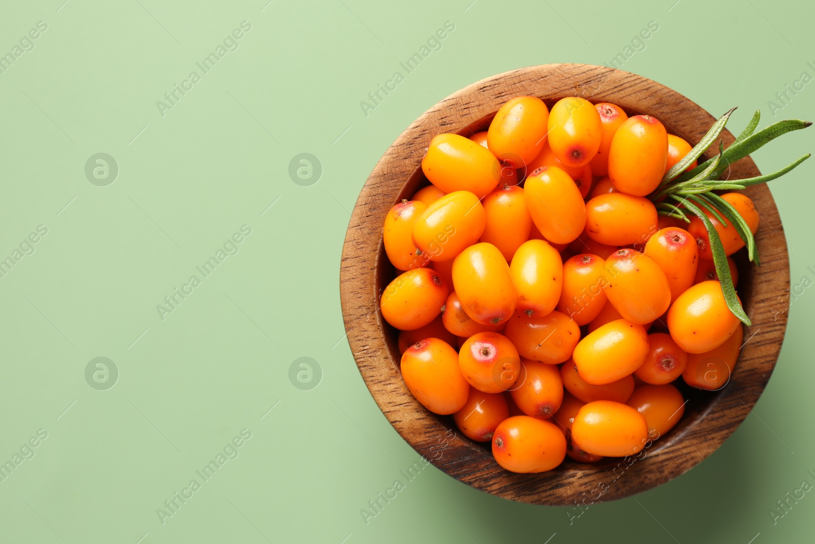 Photo of Ripe sea buckthorn berries and leaves in bowl on green background, top view. Space for text
