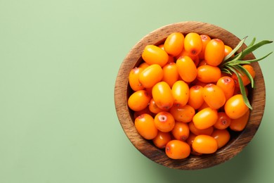 Photo of Ripe sea buckthorn berries and leaves in bowl on green background, top view. Space for text