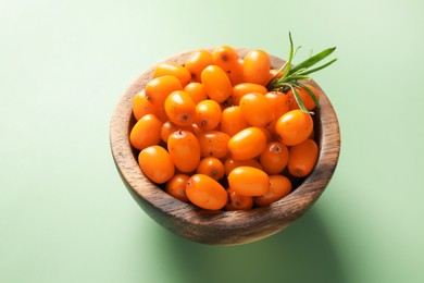 Photo of Ripe sea buckthorn berries and leaves in bowl on green background, closeup