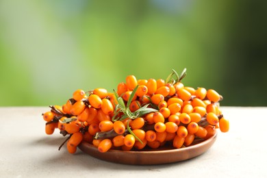 Photo of Ripe sea buckthorn berries and leaves on light table against blurred green background, closeup