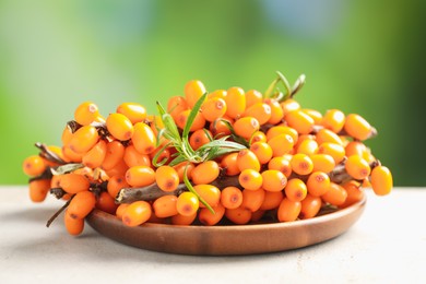 Photo of Ripe sea buckthorn berries and leaves on light table against blurred green background, closeup