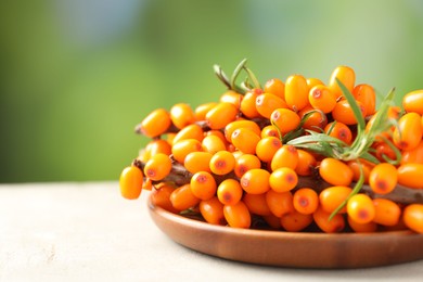 Photo of Ripe sea buckthorn berries and leaves on light table against blurred green background, closeup. Space for text