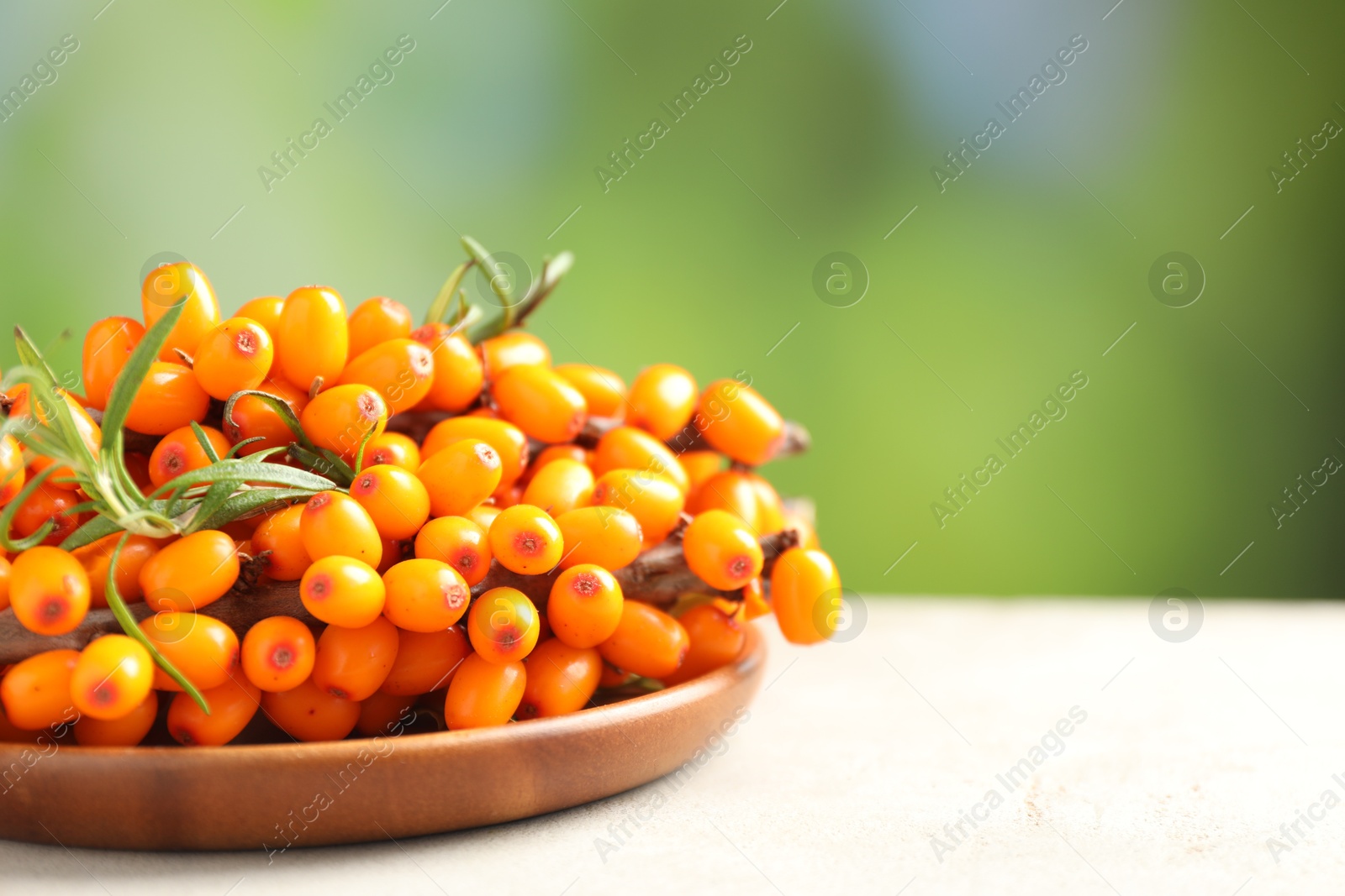 Photo of Ripe sea buckthorn berries and leaves on light table against blurred green background, closeup. Space for text