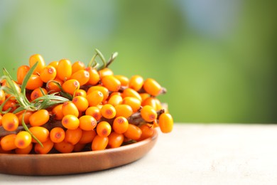 Photo of Ripe sea buckthorn berries and leaves on light table against blurred green background, closeup. Space for text