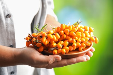 Photo of Woman with ripe sea buckthorn berries against blurred green background, closeup