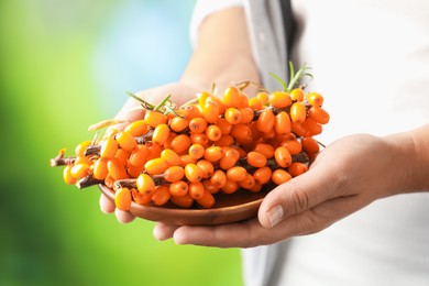 Photo of Woman with ripe sea buckthorn berries against blurred green background, closeup