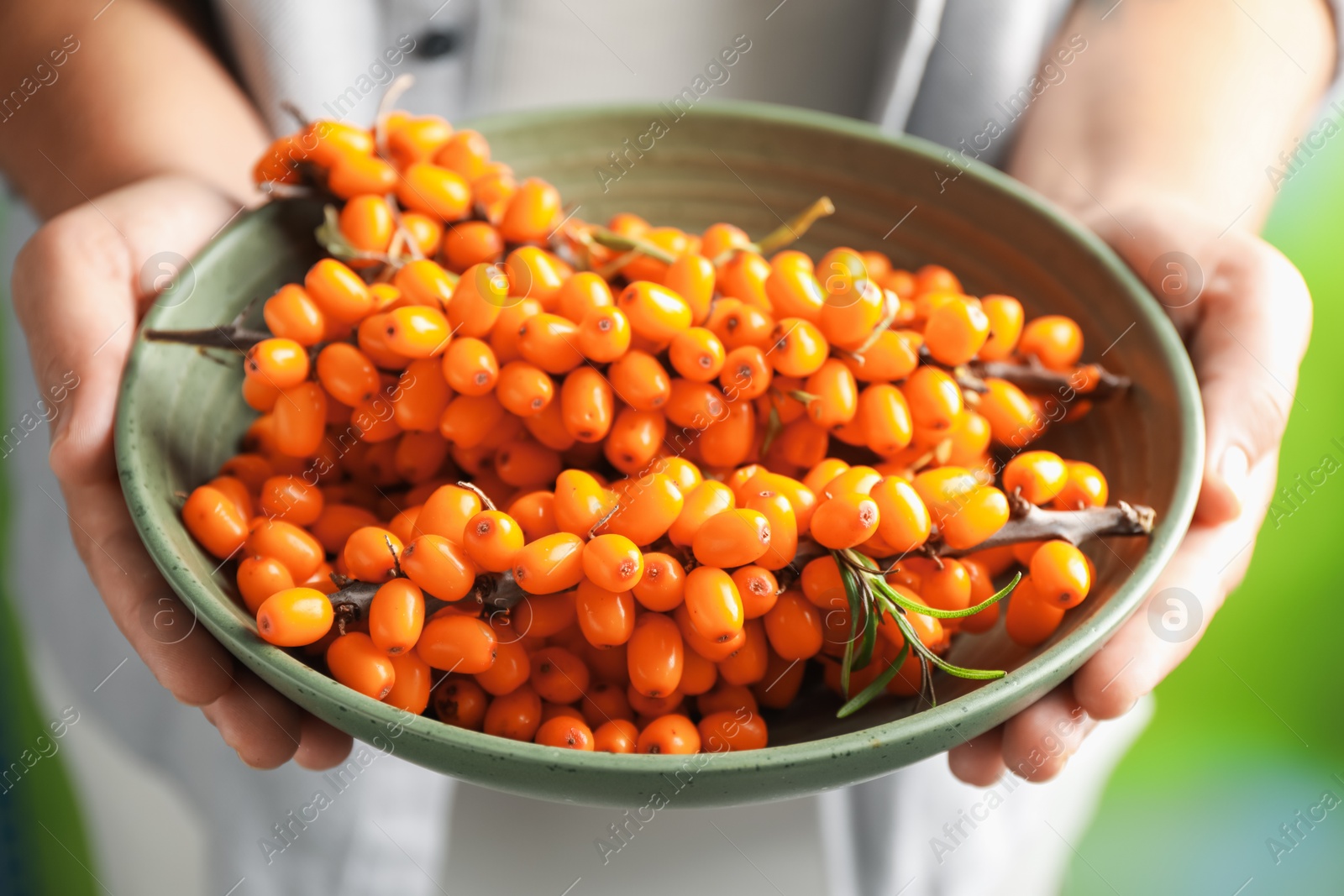 Photo of Woman with ripe sea buckthorn berries against blurred green background, closeup