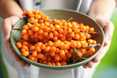 Photo of Woman with ripe sea buckthorn berries against blurred green background, closeup