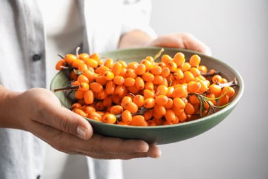 Photo of Woman with ripe sea buckthorn berries against grey background, closeup