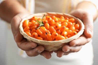 Photo of Woman with ripe sea buckthorn berries against grey background, closeup