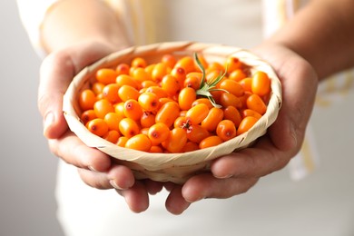 Photo of Woman with ripe sea buckthorn berries against grey background, closeup