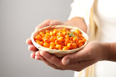 Photo of Woman with ripe sea buckthorn berries against grey background, closeup